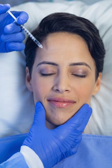 Image of a medical professional administering a facial injection to a female patient. This can be used in contexts related to cosmetic surgery, beauty treatments, or medical procedures. Ideal for articles, blogs, advertisements, and informational content on cosmetic enhancements and healthcare services.