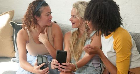 Diverse Female Friends Chatting and Relaxing on Couch with Smartphones