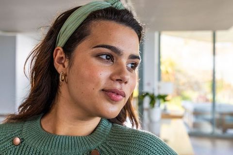 Adult woman gazing thoughtfully in bright living room wearing sage sweater and headband
