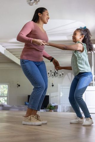 Mother and daughter spinning and laughing while holding hands on bright hardwood floor