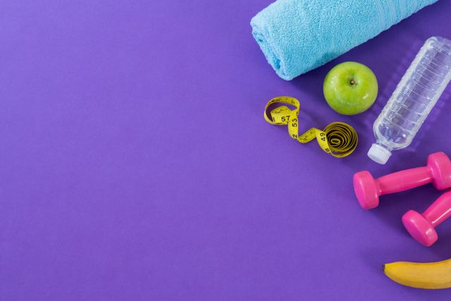 Dumbbell, apple, towel, water bottle and measuring tape on purple background