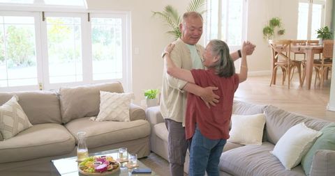 Senior couple dancing in sunlit living room embracing romantic home moment with cozy decor