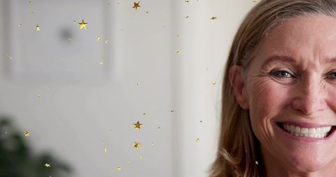 Smiling mature woman half-face portrait with gold star confetti and soft neutral background