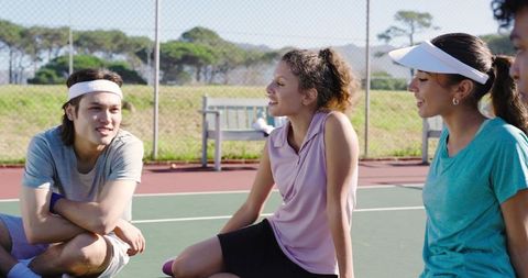Young adults chatting and laughing together on outdoor tennis court during sunny sports break