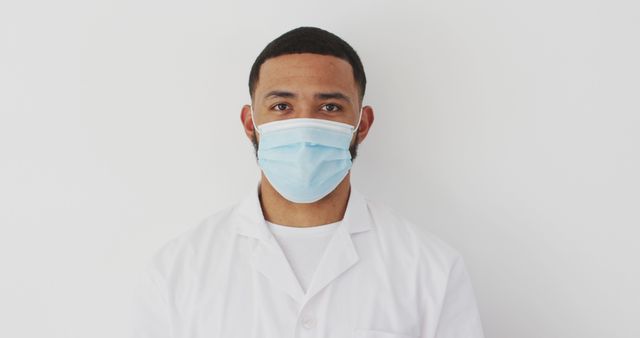 Young Male Doctor Wearing Face Mask and Lab Coat Standing Against White Background - Download Free Stock Images Pikwizard.com