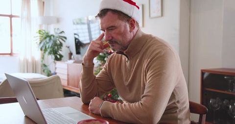 Senior man in santa hat using laptop near christmas tree at home