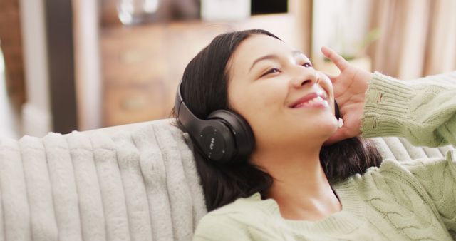 Image of smiling biracial woman with dark hair using headphones listening to music. Leisure time, domestic life and wellbeing lifestyle concept.