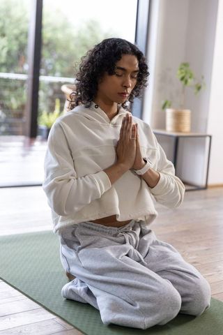 Nonbinary person practicing mindful meditation at home, kneeling on green yoga mat