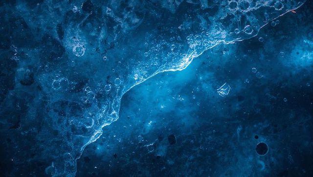 Glowing crystal ridge cutting through icy blue macro texture with luminescent bubbles