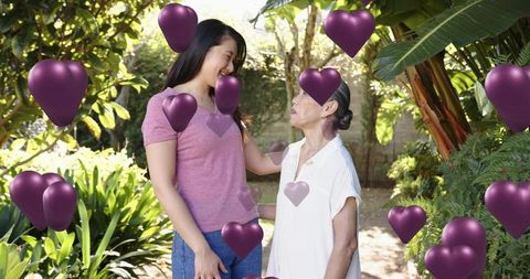 Young asian woman touching senior chinese grandmother in garden with purple heart balloons