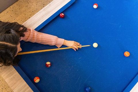Woman leaning over blue pool table aiming cue while concentrating in game room