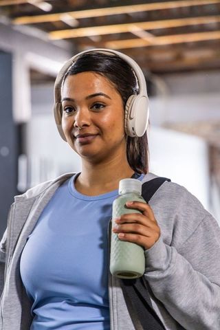 South asian woman standing at gym holding water bottle wearing hoodie and headphones