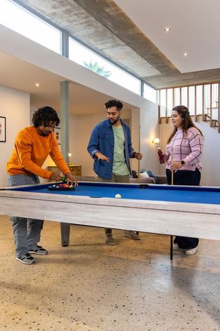 Diverse friends playing pool in modern home gameroom with blue felt table casual social