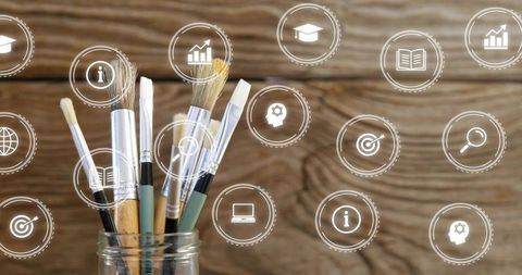 Holding paintbrushes in jar featuring education icons and analytics overlays on woodgrain