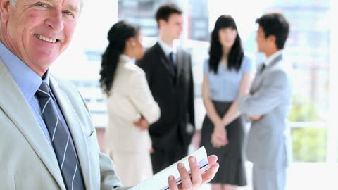 Senior Manager Reviewing Documents in Office with Team Background