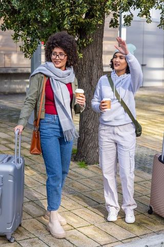 Two friends walking with rolling luggage and coffee showing casual travel and street style