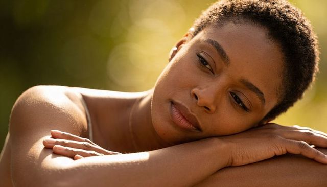 Young woman resting head on folded arms outdoors, contemplative serene close-up portrait