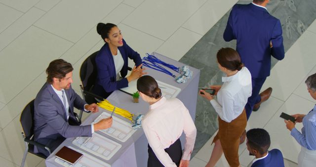 Business professionals registering at conference desk, receiving name tags, discussing details. Ideal for illustrating corporate events, networking seminars, or professional gatherings in promotional materials, presentations, and website content related to business activities and events.