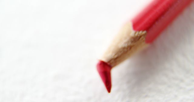 A red pencil is shown with its sharp tip in focus against a blurred white background, with copy space. Its pointed tip suggests precision, ideal for artists or writers who value detail in their work.
