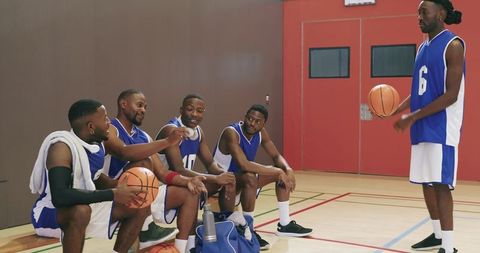 Basketball teammates chatting on bench during timeout on indoor court in blue uniforms