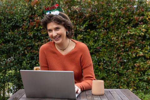 Young woman working remotely on laptop at holiday garden patio with coffee mug and headband