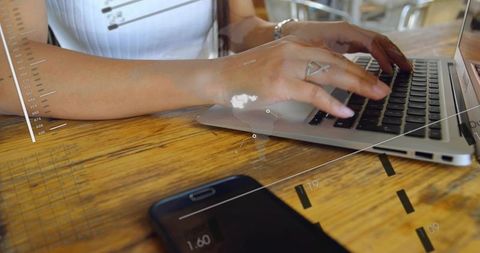 Asian woman typing on laptop with futuristic HUD overlays at cafe wooden table