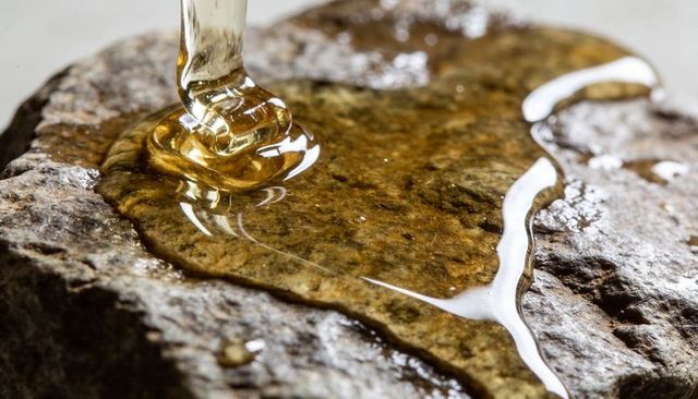 Pouring golden resin forming glossy amber puddle on rough stone slab close-up texture
