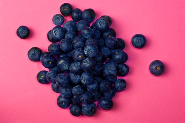 A pile of fresh blueberries spread on a vibrant pink background, highlighting their natural color and texture. Ideal for use in healthy eating campaigns, vegan recipes, summer promotions, and organic food advertisements. Great for articles on the benefits of antioxidants and nutritious snacks.