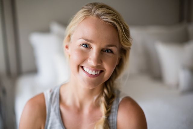 Portrait of smiling beautiful woman sitting on bed in bedroom at home