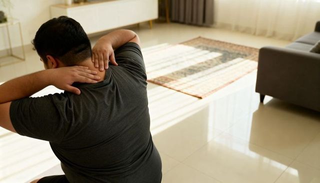 Man massaging neck while sitting on floor in modern living room with patterned rug