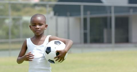 Joyful Young Boy Holding Soccer Ball Outdoors on Sunny Day