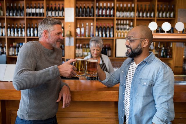 Smiling friends toasting glass of beer at counter in restaurant