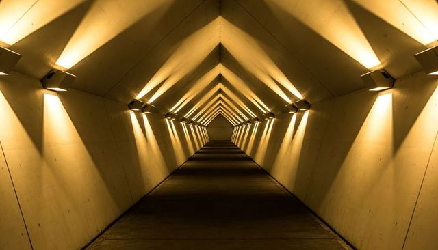 Illuminating Triangular Tunnel Corridor with Warm Sconces and Symmetrical Vanishing Point