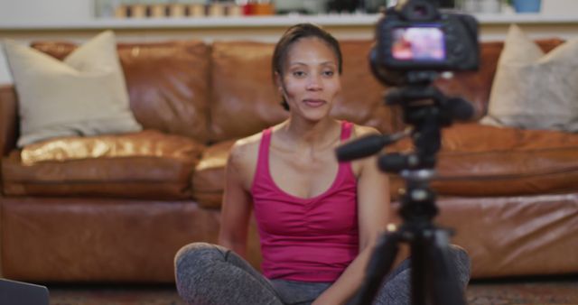 Woman sitting on the floor in front of a camera, recording a yoga tutorial. Ideal for content creators, wellness blogs, fitness and exercise programs, and lifestyle influencers promoting at-home workouts.