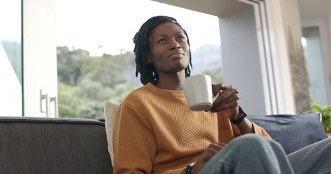Mid-adult African American man relaxing on sofa sipping coffee in modern living room