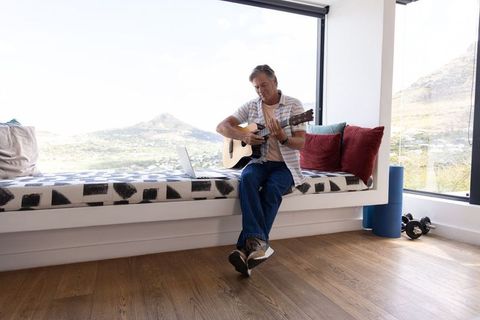 Mature man playing acoustic guitar on window bench with panoramic mountain view