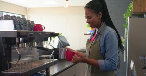African american barista pouring steamed milk for latte by commercial espresso machine