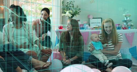 Friends chatting at baby shower holding infant with pastel decorations, cupcakes & balloons