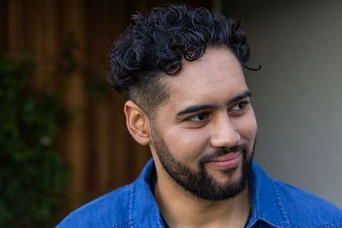 Smiling man wearing denim shirt looking right casual outdoor headshot with trimmed beard