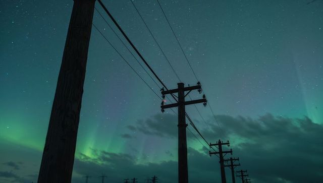 Wooden utility poles stretching into night with green aurora illuminating starry sky