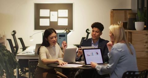 Diverse Professionals Discussing Data on Laptops in Modern Office