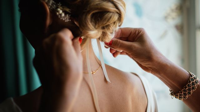 A close-up of a woman's hands fixing a bride's hair as she prepares for her wedding. This image can be used for wedding planning websites, bridal magazines, and articles focusing on wedding preparation and hairstyling tips.