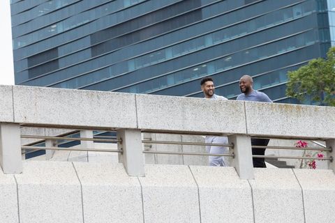 Two african american men walking and laughing on urban concrete bridge with planter