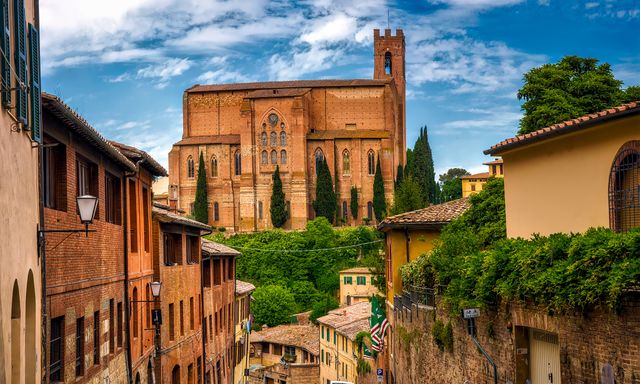 Ancient brick cathedral rising above picturesque streets of Siena, Italy. Perfect for travel blogs, history articles, and European tourism advertisements highlighting medieval architecture and cultural heritage locations.