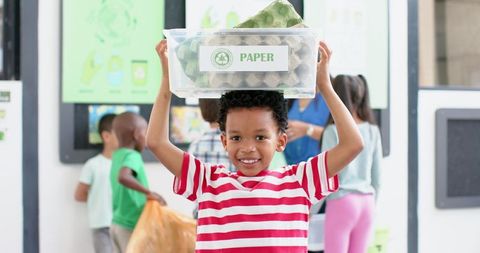 Smiling boy holding recycling bin during school recycling activity
