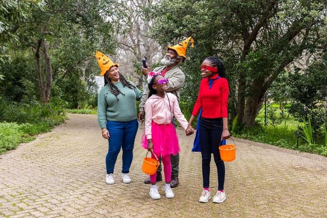 African american family wearing pumpkin hats walking park for halloween trick-or-treating