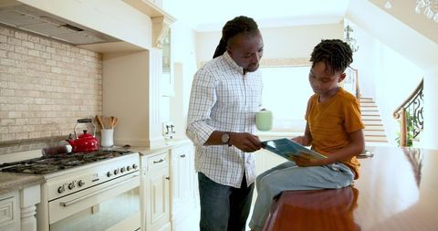 Father Sharing Storybook with Smiling Son in Bright Kitchen