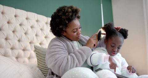 Mother and Daughter Brushing Hair Together on Bed