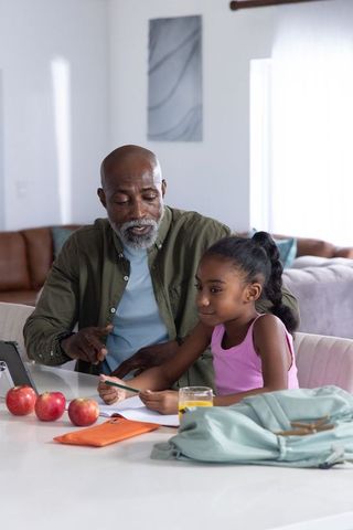 Senior african american man helping young girl with homework, pointing at tablet