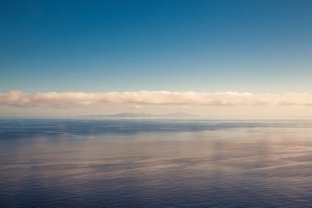 Calm sea meeting sky with a serene horizon and distant clouds. Peaceful view of the ocean during calm weather, ideal for travel, nature, and relaxation themes. Suitable for backgrounds promoting tranquility, reflection, and enhancing a sense of space in creative projects.